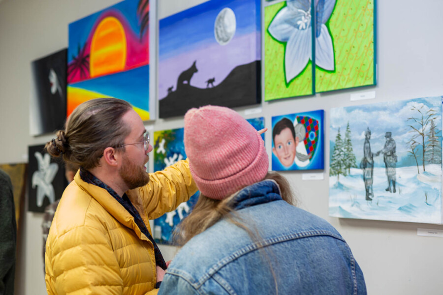 Two people looking at the artwork on a wall at an exhibition and talking 