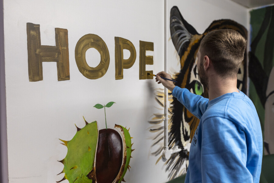 A person in custody paints 'Hope' on the wall, part of a larger decorative mural