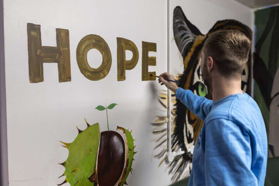 A man paints the word 'Hope' on the wall alongside images of a tiger and a conker