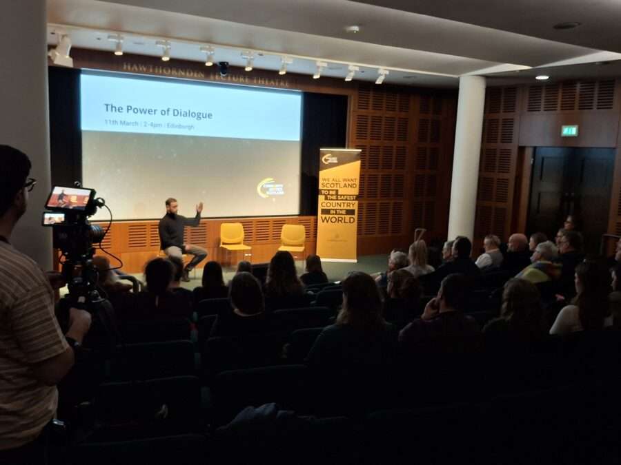 A dark auditorium; a seated audience watching a presentation