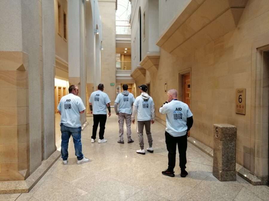 Five people standing in a court entranceway with their backs to the camera. Their t-shirts show the Aid & Abet logo.